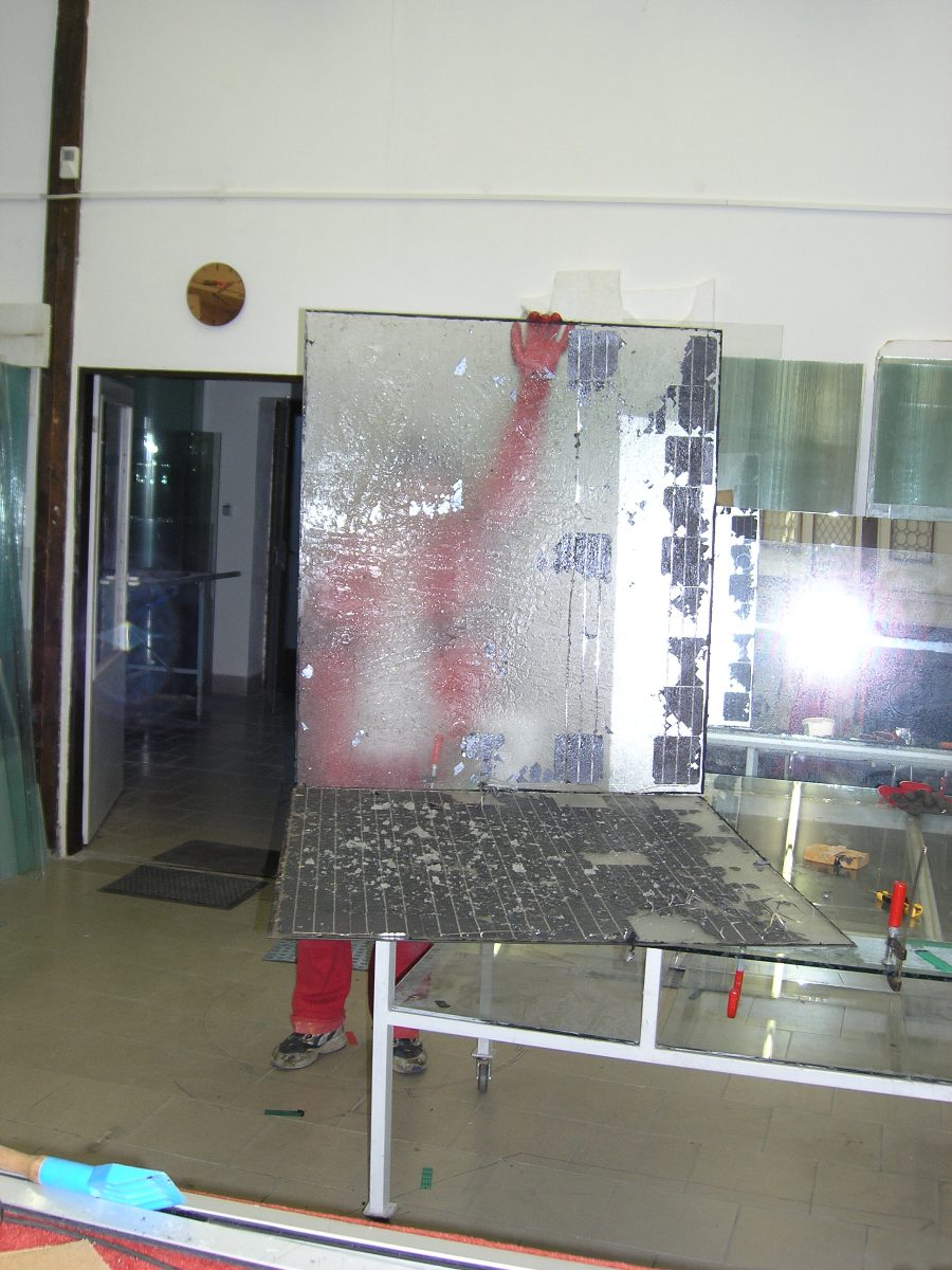 Worker lifting a partially delaminated panel off the glass, cells separating from the laminate.