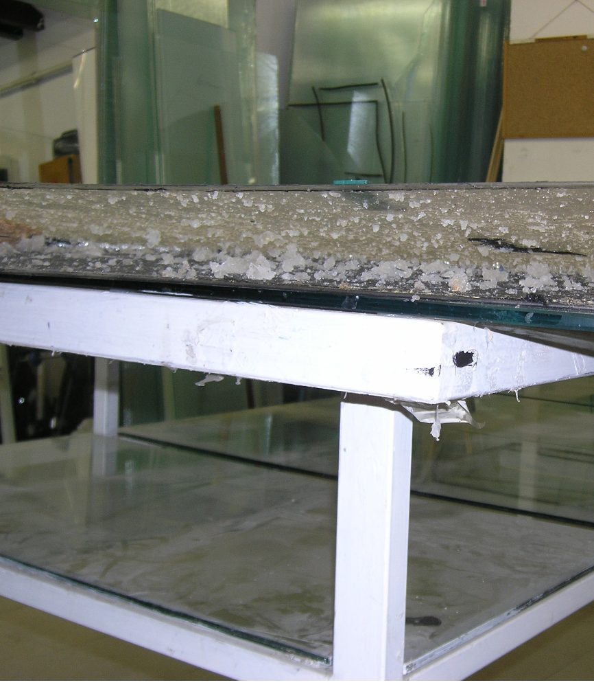 Edge of a silicone-gel panel being separated — softened gel lifts off the glass, with clean recovered glass sheets stacked beneath.
